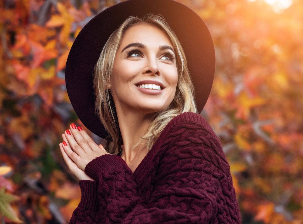 Woman wearing a hat with sun and trees in the background.