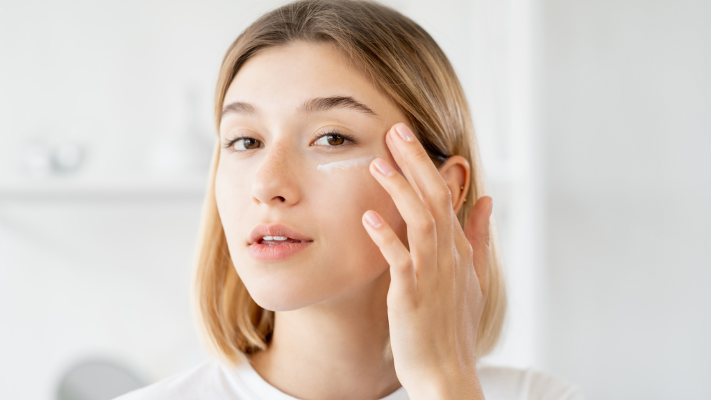 Young woman applying skincare cream under her eye with her finger.