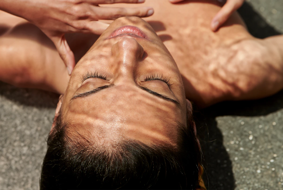 Person lying on their back, eyes closed, with shadows across their face and skin