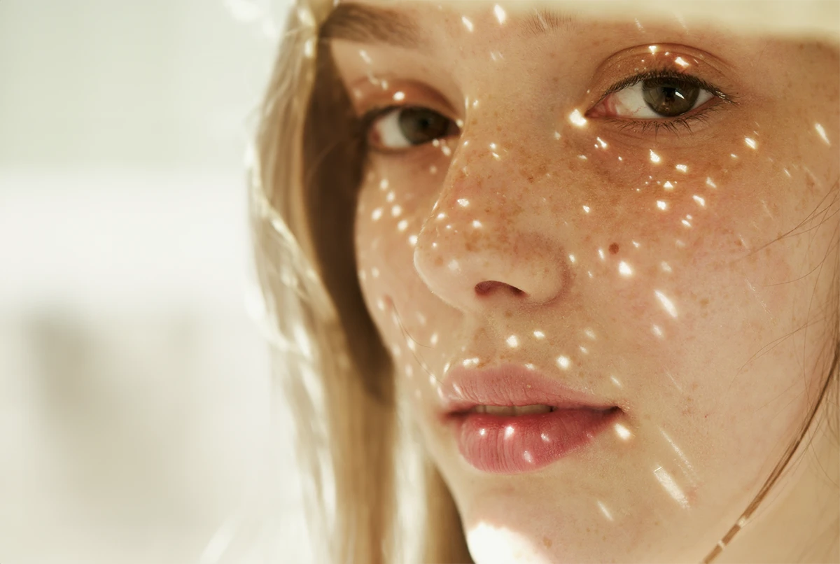 Close-up of a woman's face with freckles, illuminated by light spots