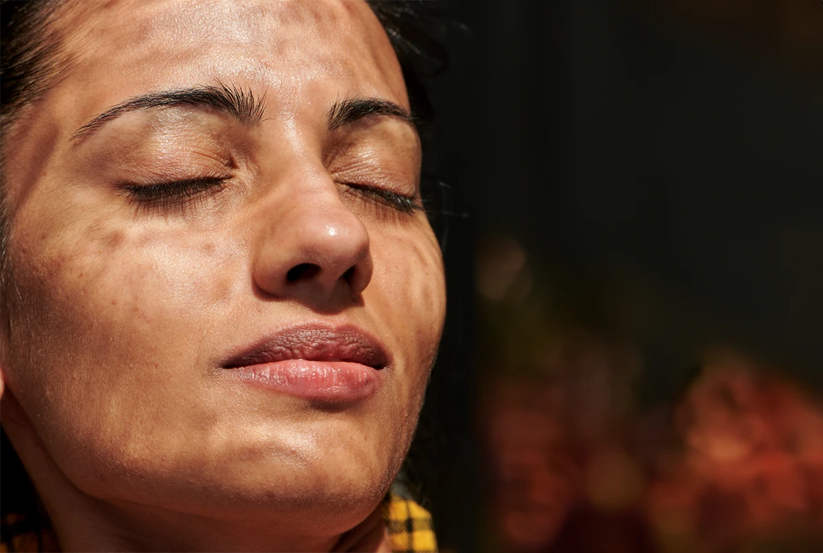 Close-up of a woman with eyes closed, light patterns on her face, neutral background