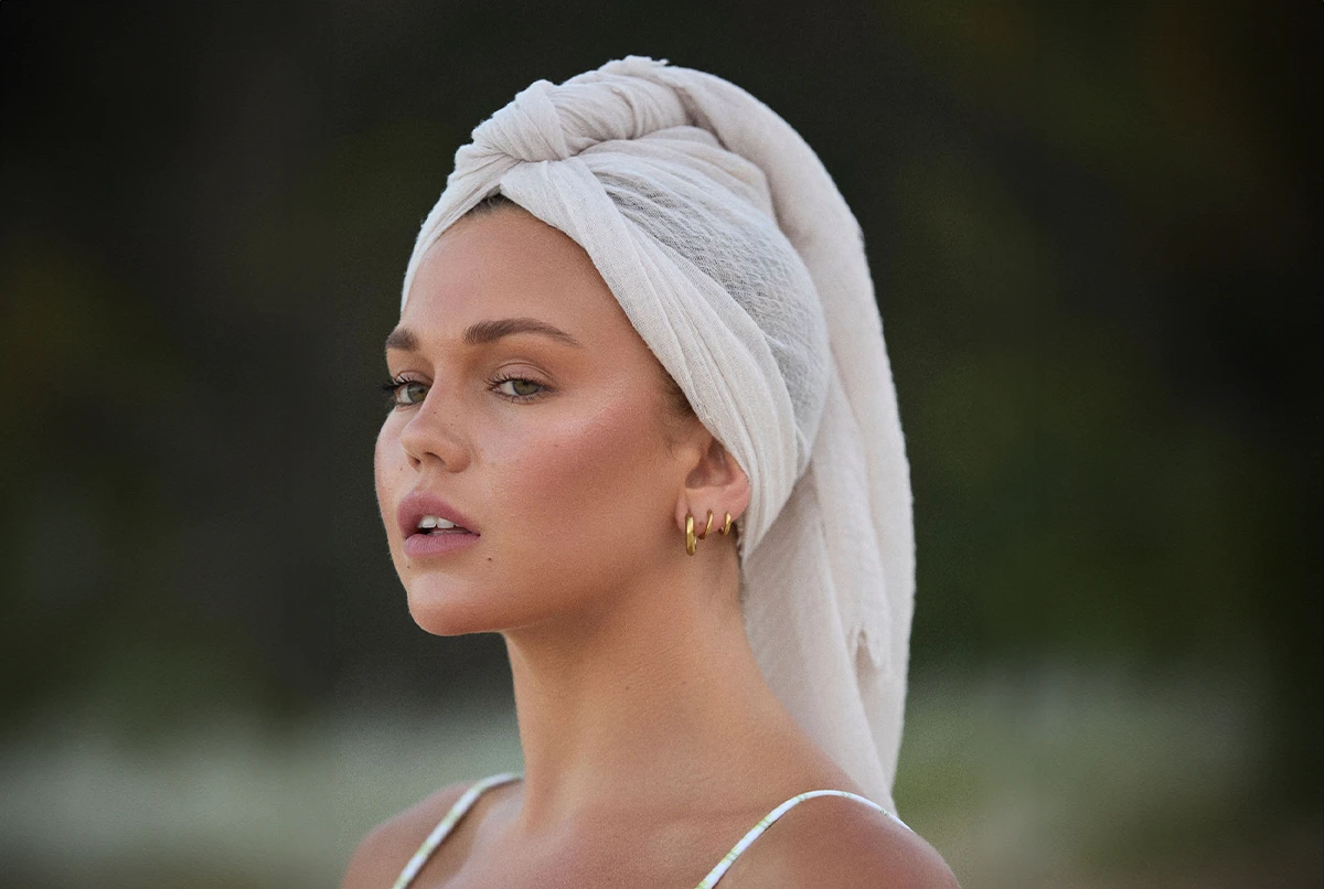 Profile of a person with a towel wrapped on their head, wearing earrings