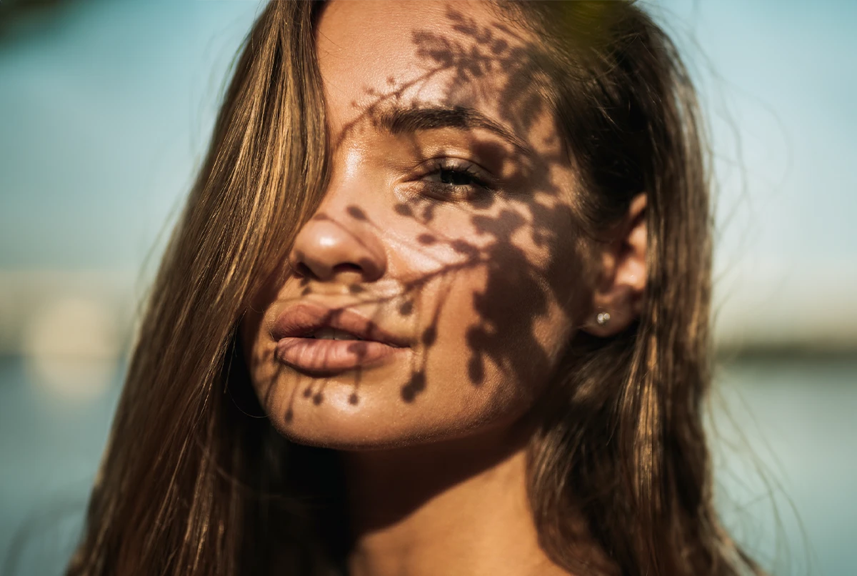Close-up of a woman's face with sunlight casting a leaf pattern shadow over her skin
