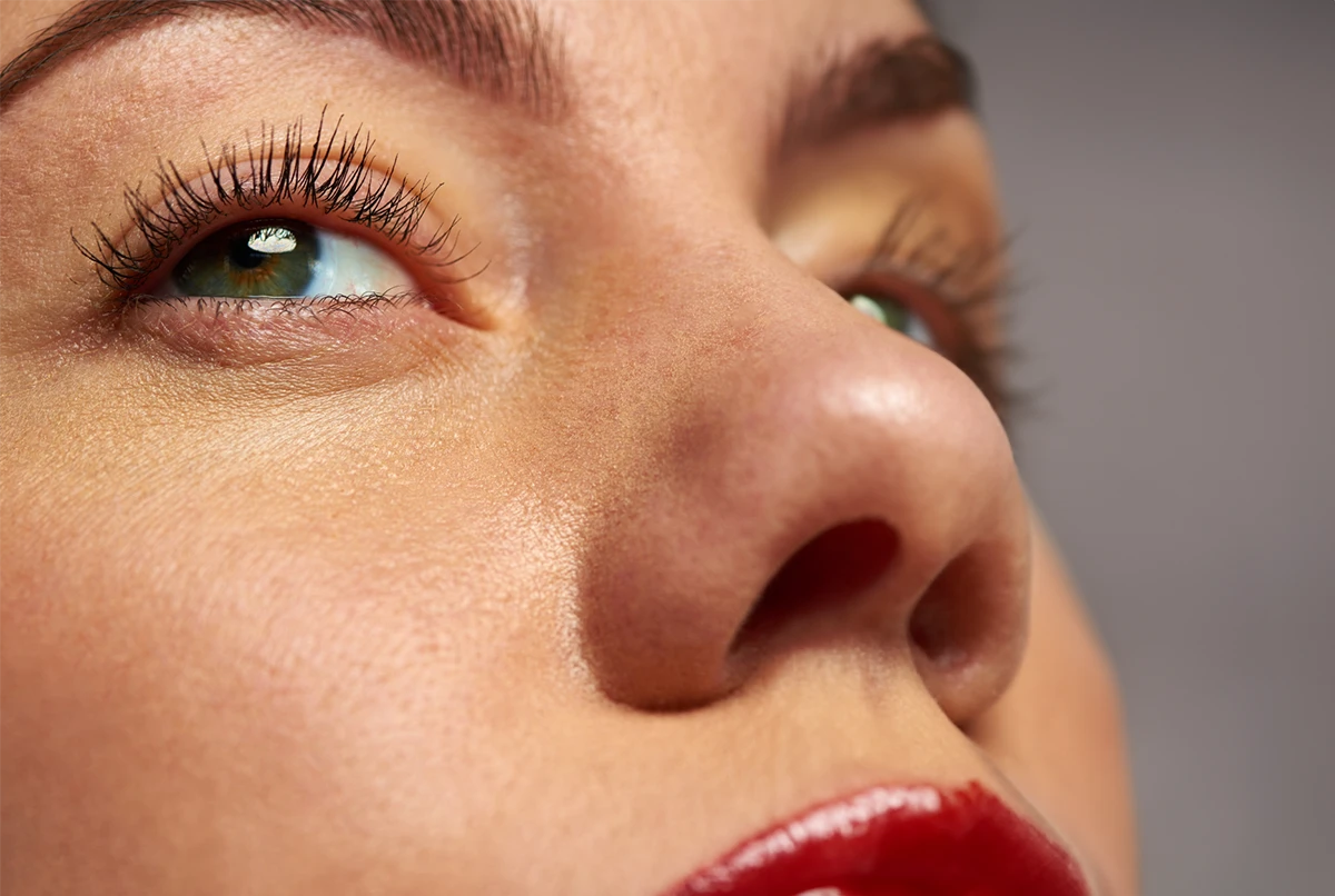 Close-up of a woman's face focusing on her eye, nose, and lips with red lipstick