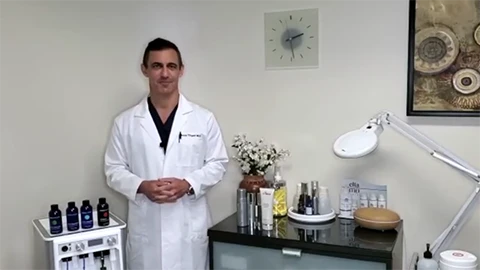 A person in a lab coat stands next to a treatment station with skincare products