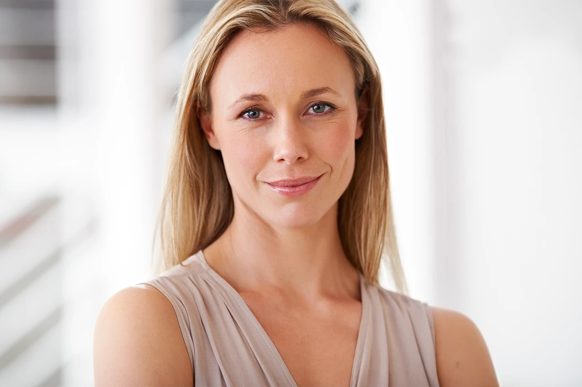 A woman with long blonde hair and blue eyes, smiling softly in a light environment