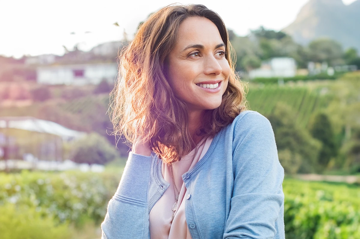 Smiling woman with wavy hair standing outdoors in a green landscape