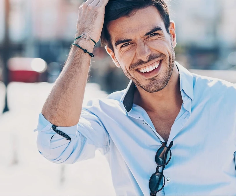 Man smiling and touching his hair, wearing a light blue button-up shirt and sunglasses