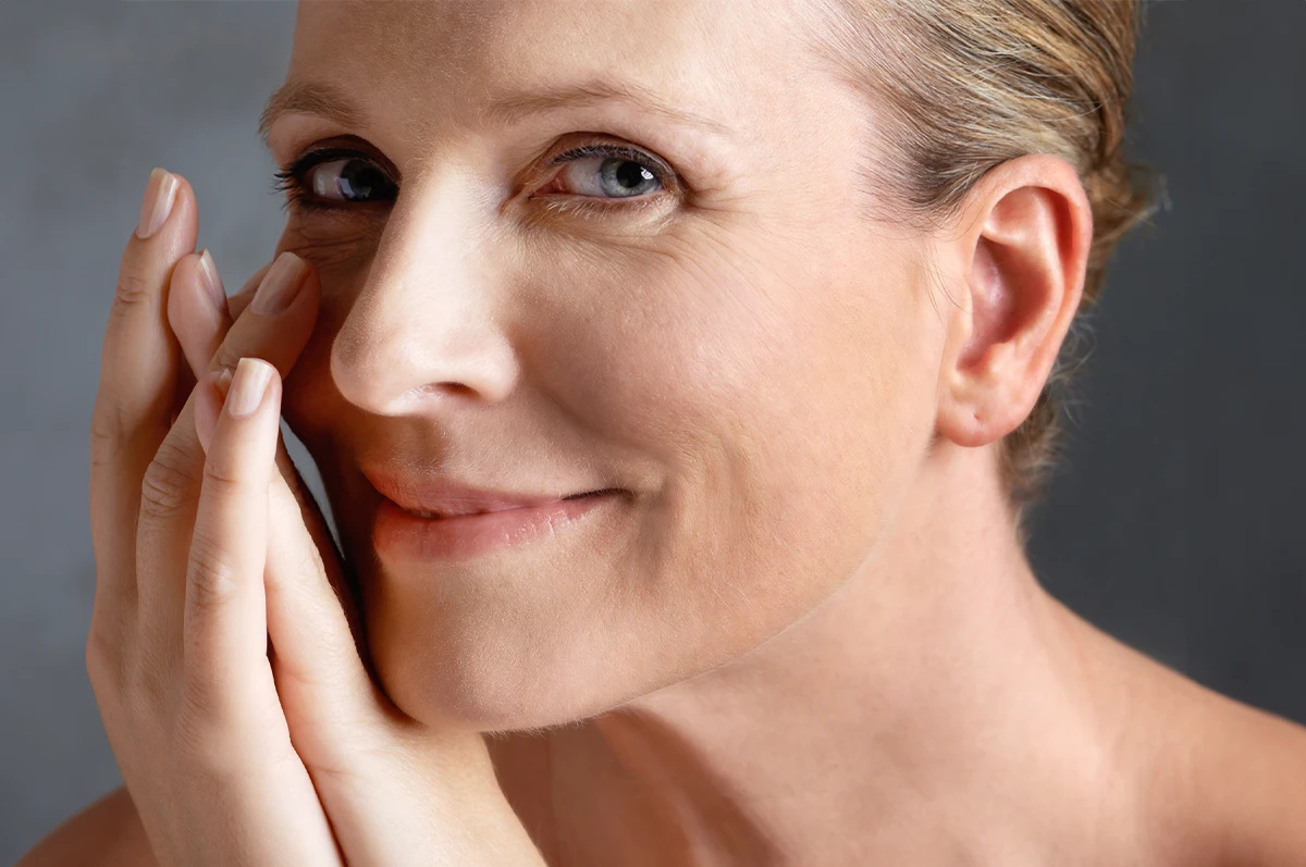 Woman smiling softly, resting her chin on one hand, with hair pulled back