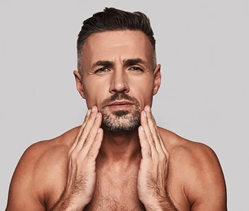 Man with short hair and a beard touching his face, against a gray background