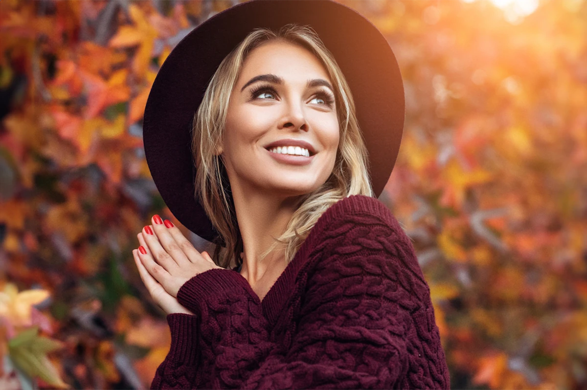 Woman smiling, wearing a hat, with autumn leaves in the background