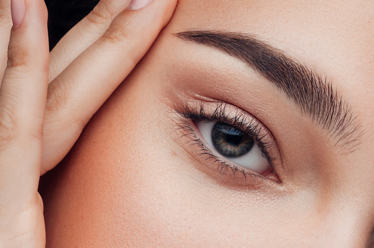Close-up of a woman's eye with well-groomed eyebrows and hand touching her face