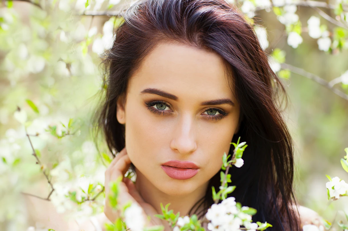 Close-up of a woman with dark hair, surrounded by blooming flowers