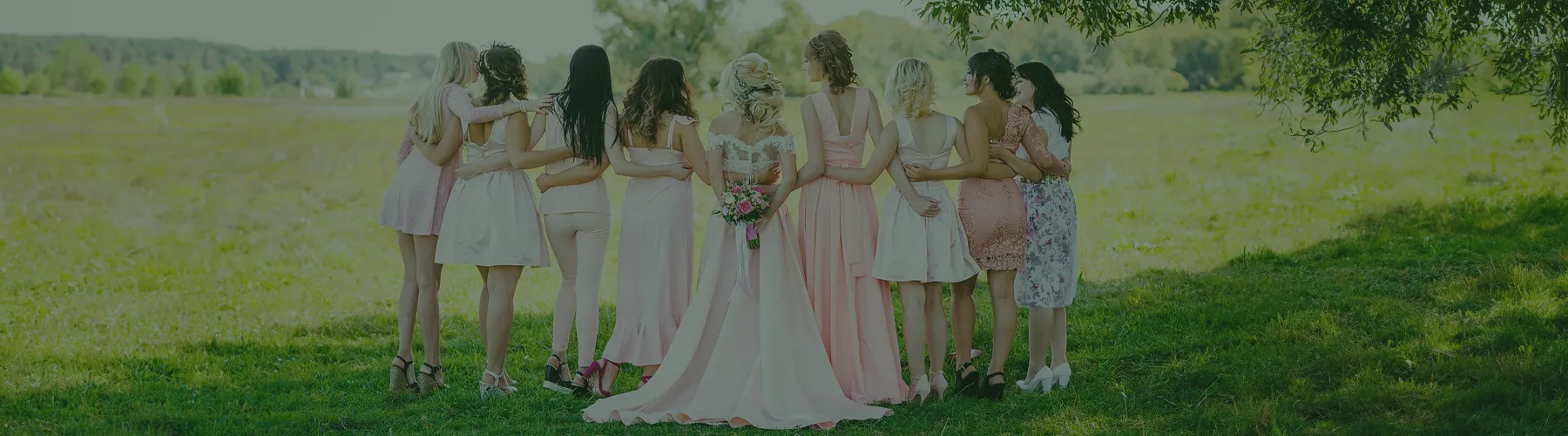 A group of women standing together in a field, some in dresses, holding flowers