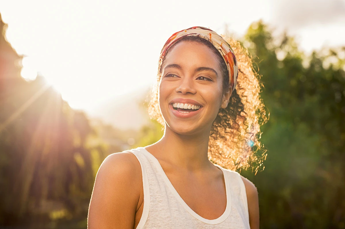 Smiling woman with curly hair and a headband, outdoors in sunlight