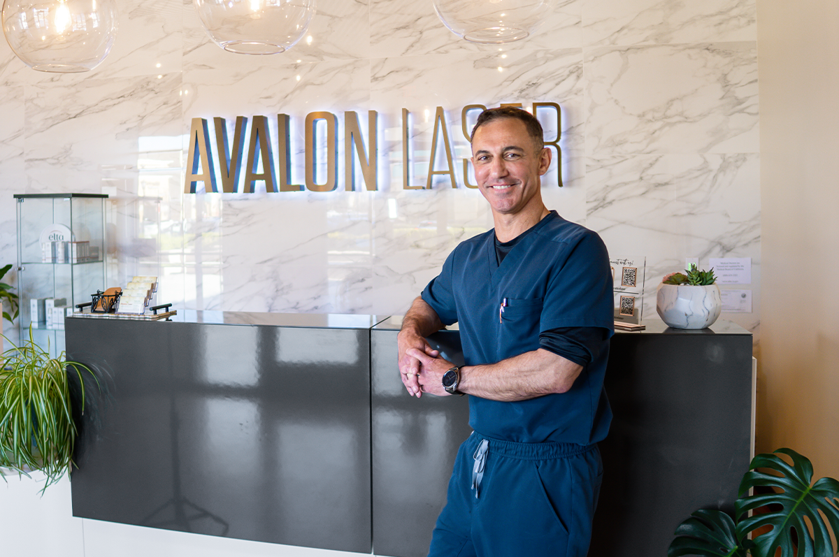 A man in scrubs stands by a reception desk with a sign in a modern, bright space
