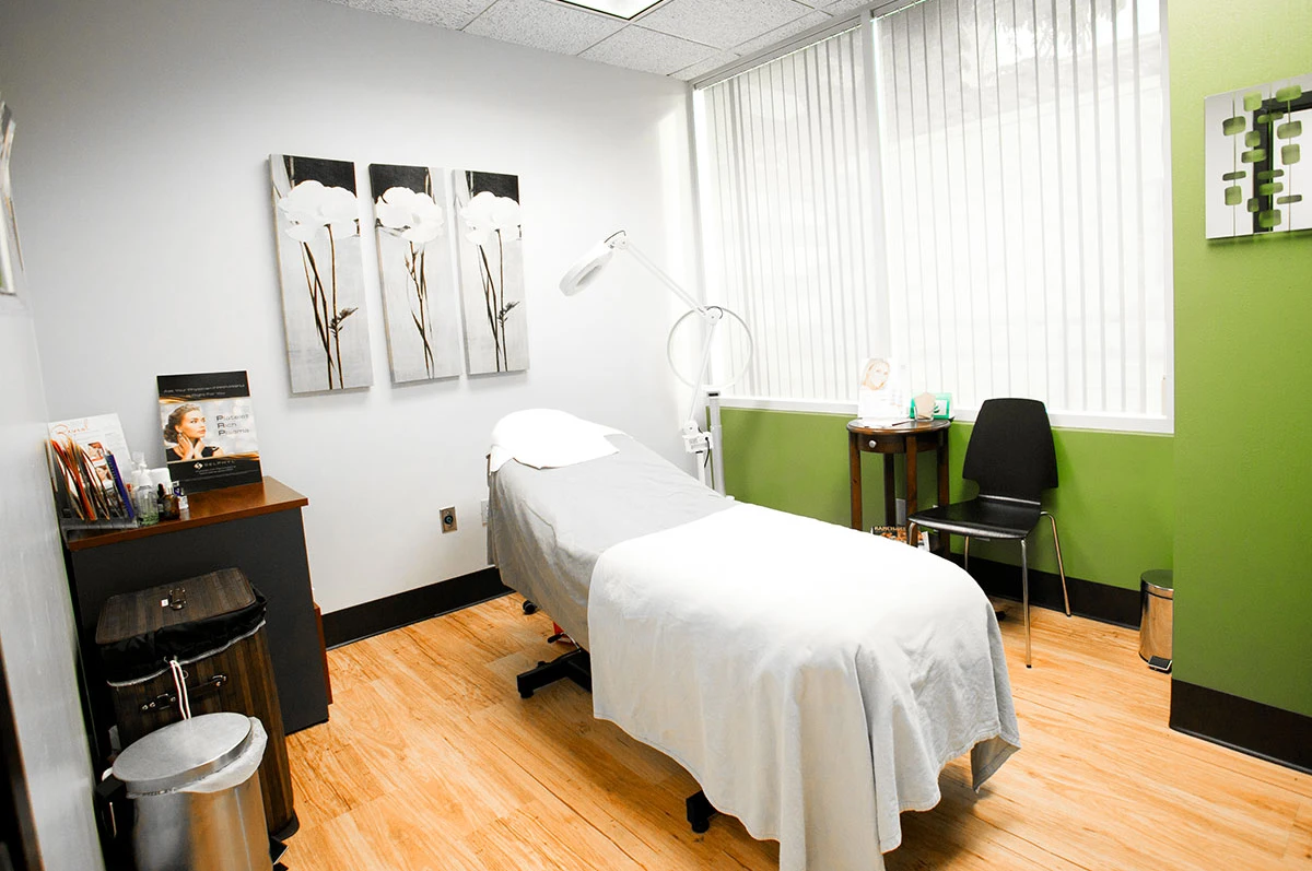 Treatment room with a bed, chair, and artwork on the walls. Bright window light