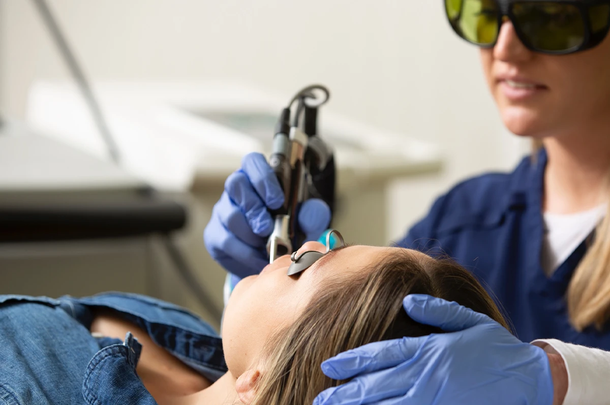 A patient lies back as a clinician uses a laser tool in a dental setting