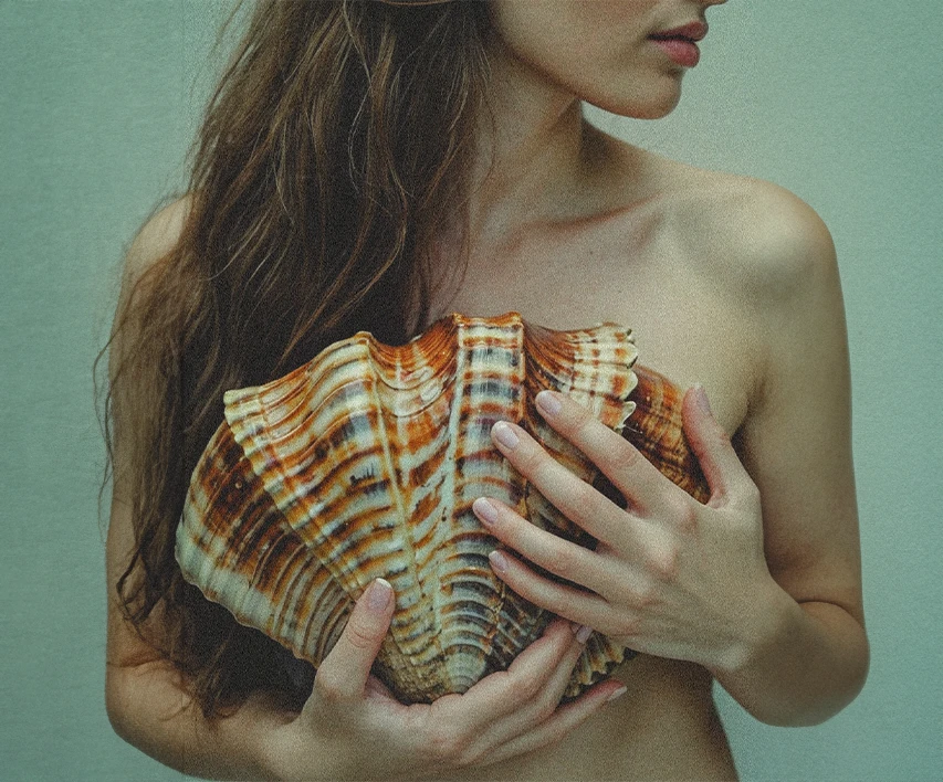 A woman holds a large shell in front of her chest, with long hair partially covering her shoulder