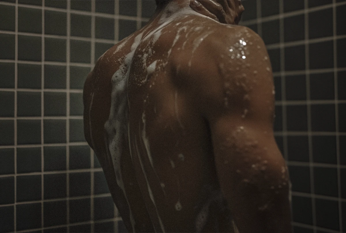 A person in a shower with water and soap on their back, facing away from the camera